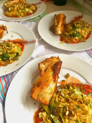 Knuspriges Fischgericht mit Gemüse Mehrere Teller mit Nudeln, Gemüse und gebratenem Fisch, garniert mit Sauce.